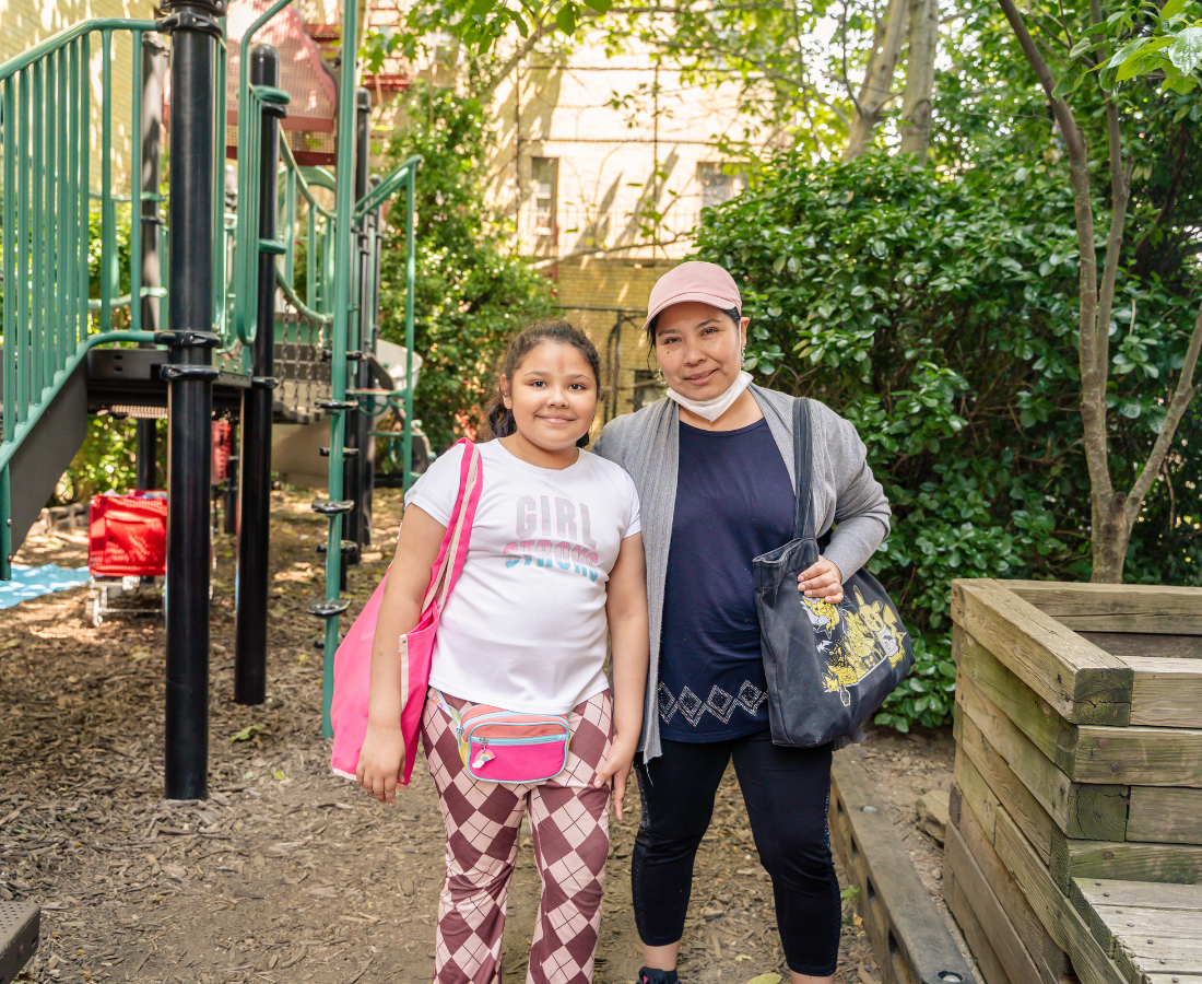 A mother and daughter smile in front of the playground structure at Creston Ave Community Playground