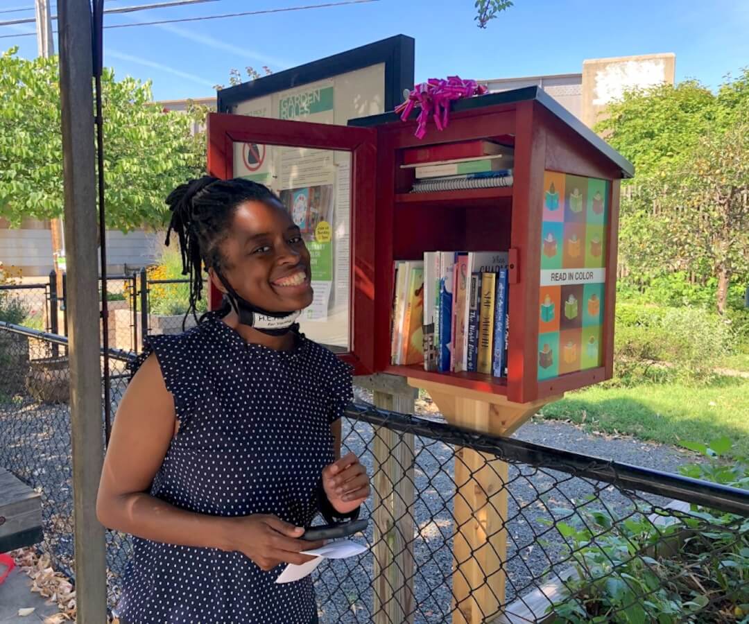 person smiling with little free library at community garden